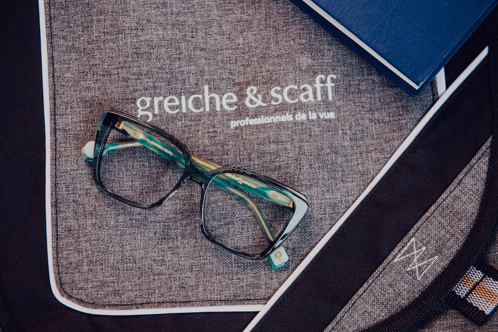 Green eyeglasses displayed on a Greiche & Scaff cloth